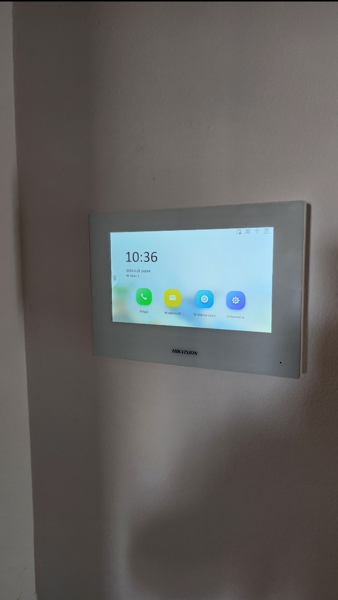 Panel dotykowy domofonu Hikvision zamontowany na ścianie, wyświetlający ekran główny z ikonami połączeń, wiadomości, podglądu na żywo i ustawień.