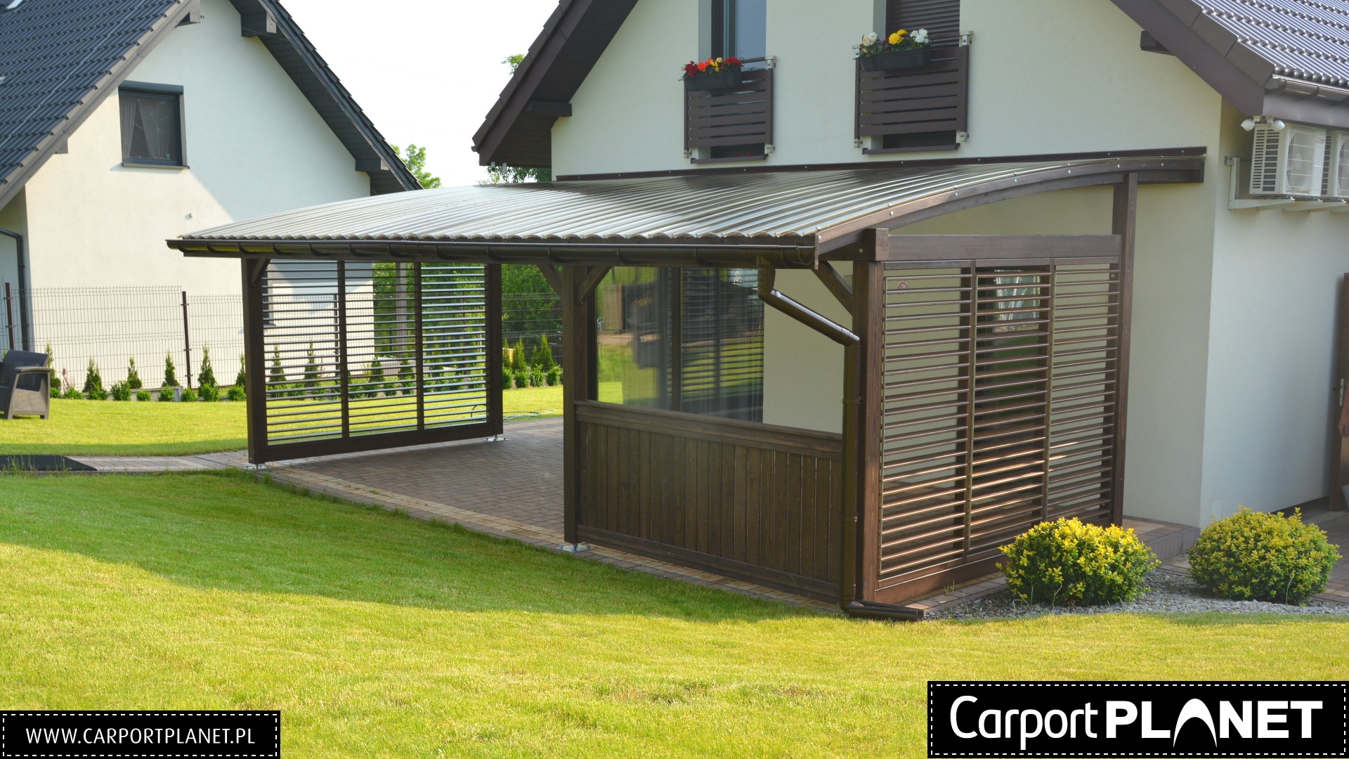 Nowoczesna konstrukcja z metalowym zadaszeniem i drewnianymi lamelami, przylegająca do domu z zielonym trawnikiem.