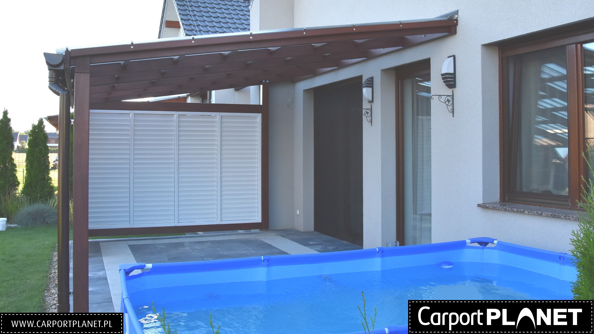 Ciemnobrązowa pergola drewniana z białymi żaluzjami osłaniająca taras z basenem stelażowym przy domu.