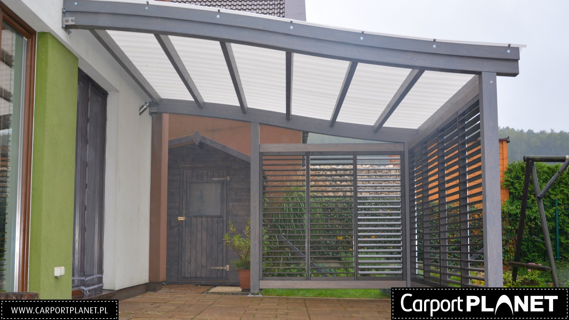 Zadaszenie z drewnianą konstrukcją i lamelami, przylegające do budynku z zielonym akcentem, obok drewniana budka narzędziowa i rośliny w doniczce.