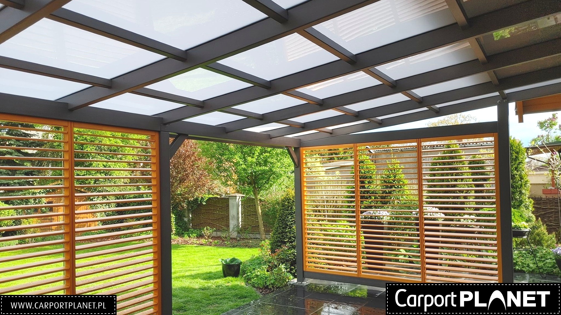 Zadaszona konstrukcja z metalowym szkieletem i drewnianymi żaluzjami na tle zielonego ogrodu, widok z wnętrza.