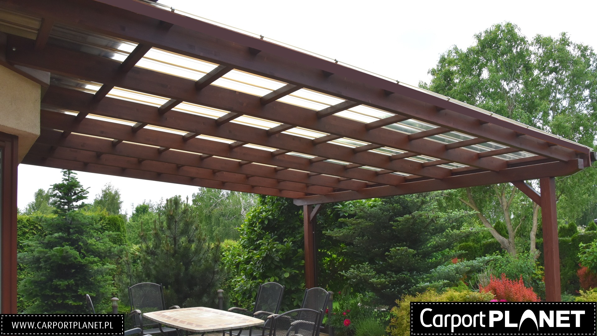 Zadaszona drewniana konstrukcja nad tarasem z przezroczystym dachem, widok na ogród z roślinnością.