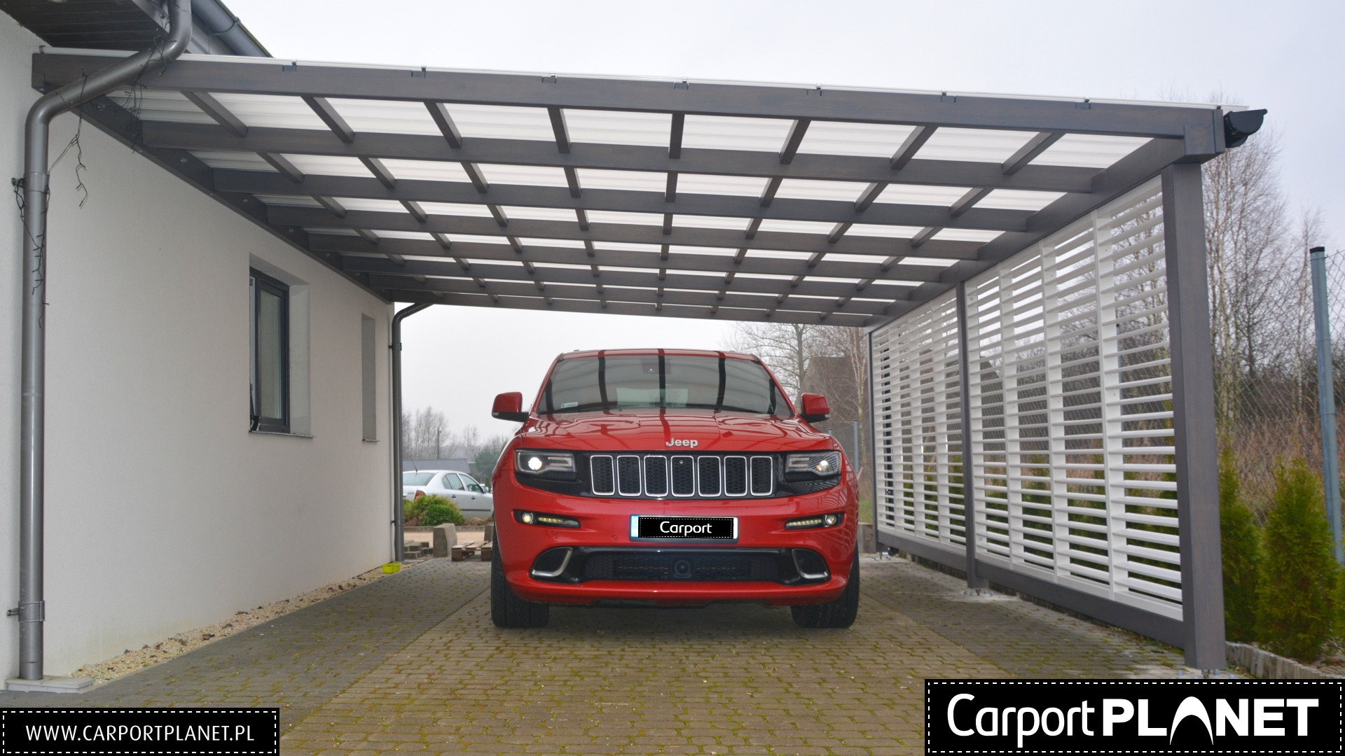 Nowoczesna metalowa pergola z ażurową ścianą boczną, osłaniająca czerwony samochód Jeep na brukowanym podjeździe.