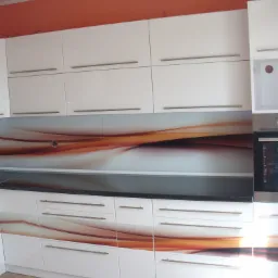 Nowoczesna zabudowa kuchenna w Radomsku z białymi frontami, ciemnym blatem i szklanym panelem dekoracyjnym z motywem abstrakcyjnych brązowo-pomarańczowych fal.