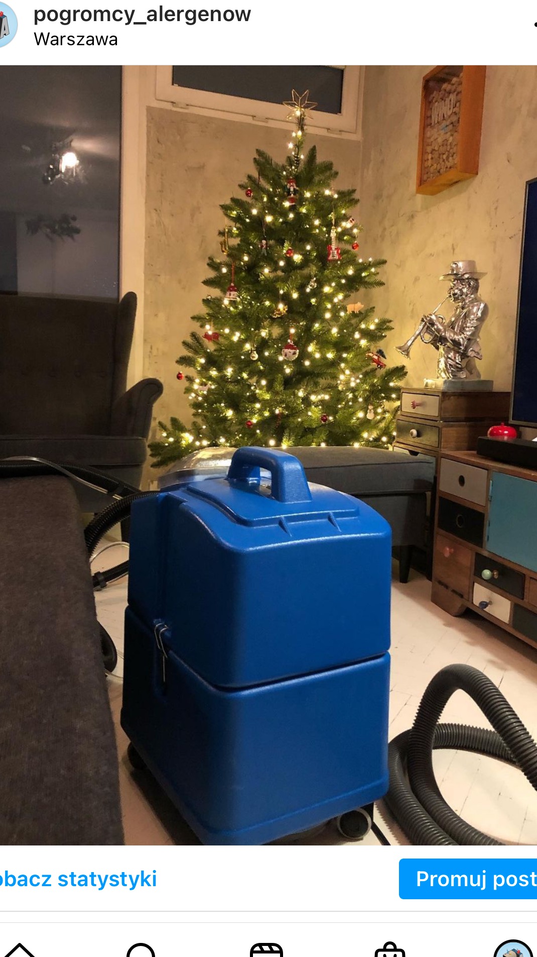 Niebieski odkurzacz piorący na tle świątecznej choinki i mebli w eklektycznym stylu.