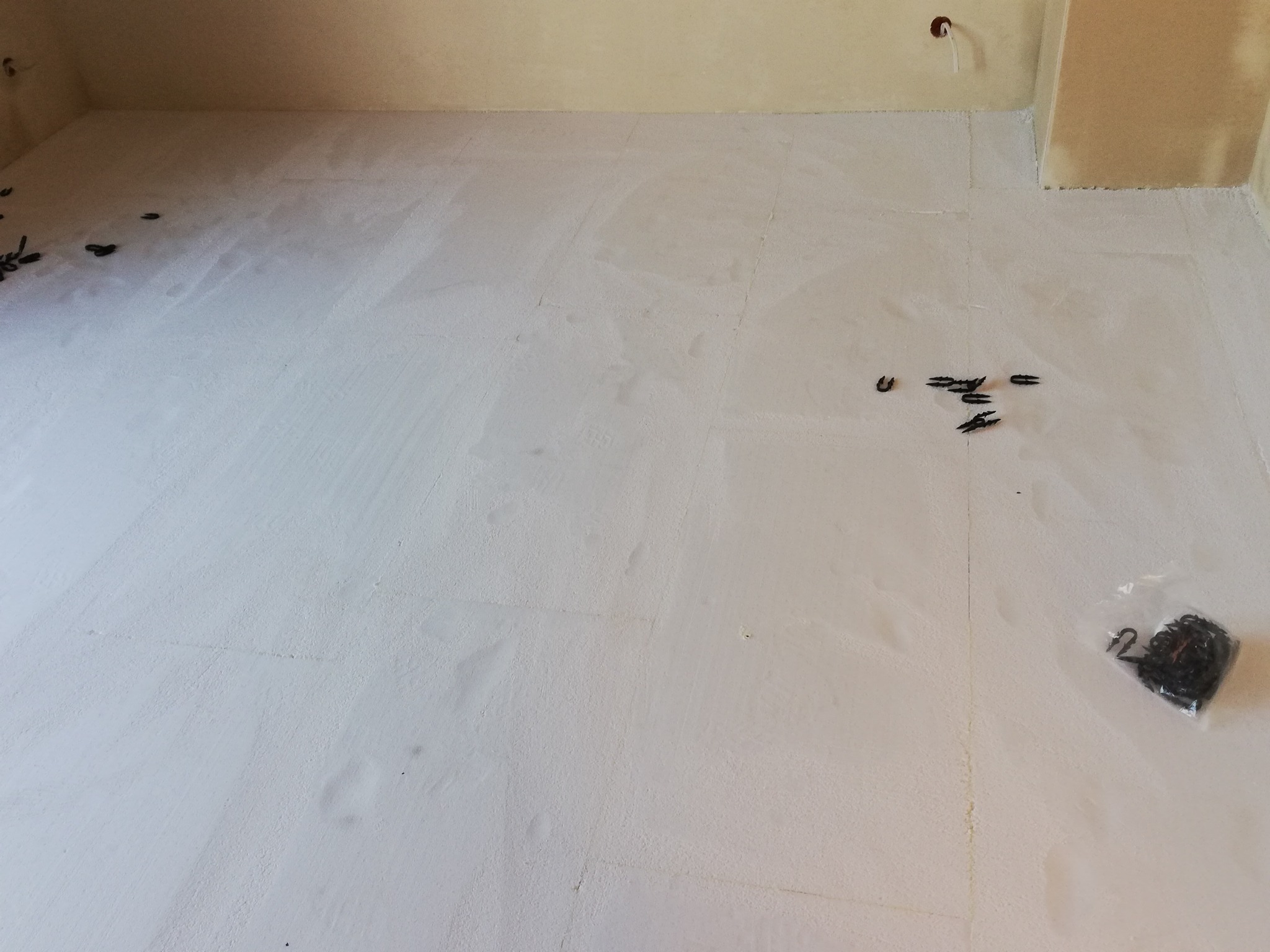 Biała izolacja podłogowa EPS z rozłożonymi klipsami mocującymi i paczką klipsów w folii, przygotowana do dalszych prac.