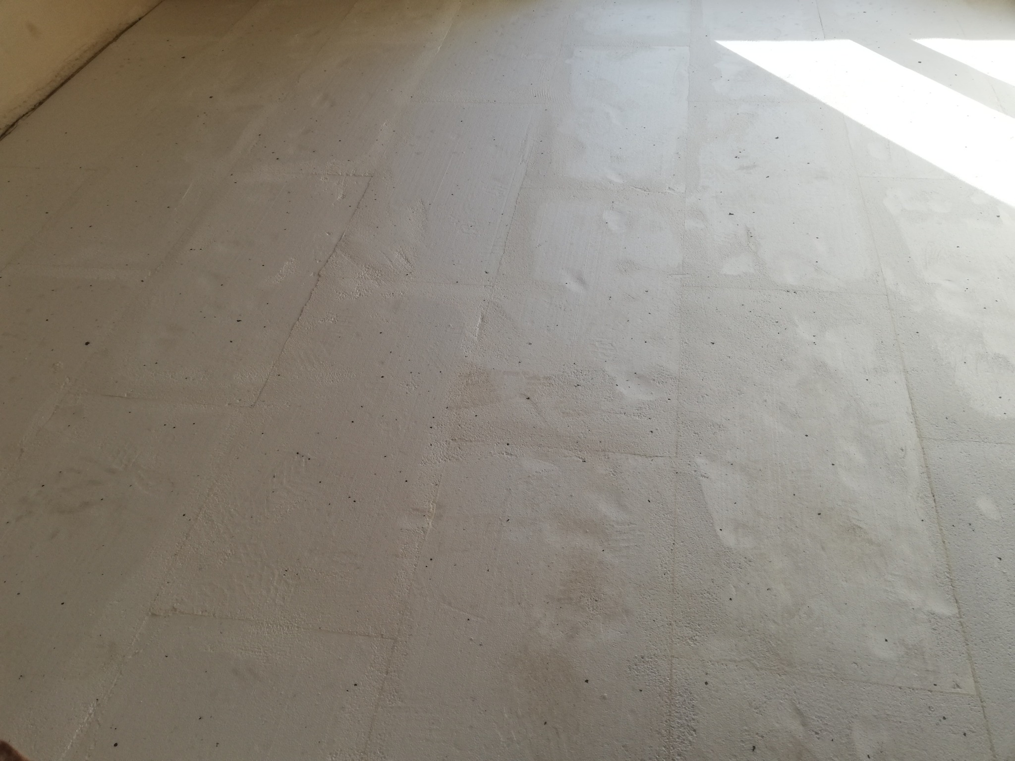 Świeżo wylana, jasna wylewka betonowa na podłodze w Nowym Dworze Mazowieckim, z widocznymi śladami po szpachli i delikatnym cieniowaniem od światła słonecznego w rogu pomieszczenia.