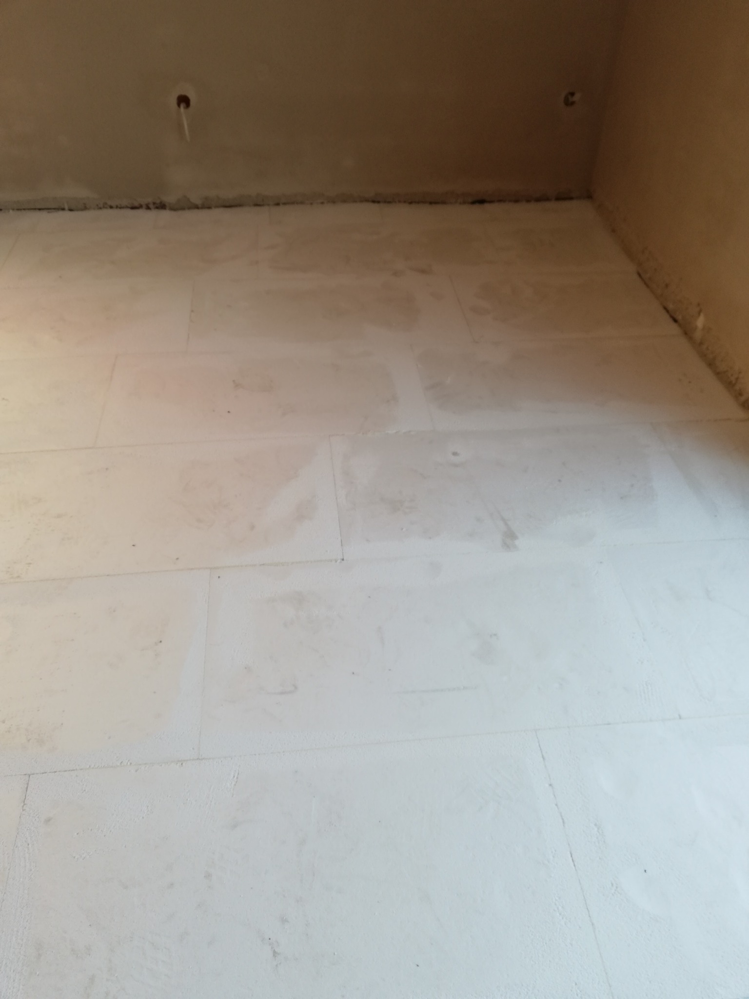 Surowy, betonowy podkład pod posadzkę z widocznymi śladami szpachlowania i instalacjami w suficie, przygotowany do dalszych prac wykończeniowych.