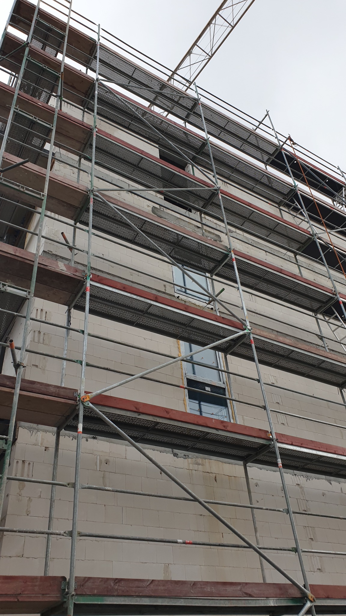 Budynek w trakcie prac elewacyjnych, widoczne rusztowania i surowa ściana z pustaków.