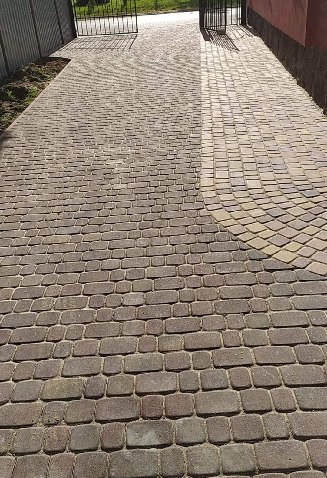 Ułożona kostka brukowa w odcieniach brązu i beżu, tworząca wzór łuku przy bramie wjazdowej, widok z góry.