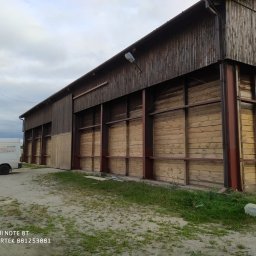 KOLORTEK - TOMASZ TWARDOSZ - Drewniany budynek gospodarczy po piaskowaniu, z widoczną różnicą w kolorze drewna. Częściowo odnowiona elewacja i zaparkowany bus firmy.