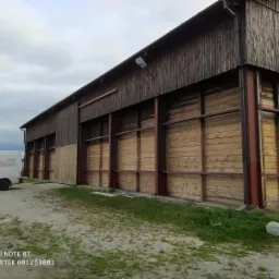 Drewniany budynek gospodarczy po piaskowaniu, z widoczną różnicą w kolorze drewna. Częściowo odnowiona elewacja i zaparkowany bus firmy.