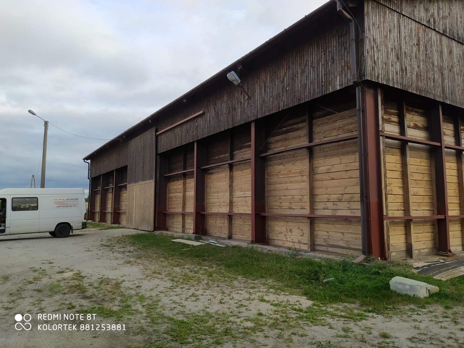 Drewniany budynek gospodarczy po piaskowaniu, z widoczną różnicą w kolorze drewna. Częściowo odnowiona elewacja i zaparkowany bus firmy.