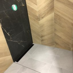 Matmal - Nowoczesna kabina prysznicowa z czarną ścianą imitującą marmur, drewnopodobnymi płytkami ułożonymi w jodełkę na sąsiedniej ścianie i szarymi płytkami na podłodze z odpływem liniowym.