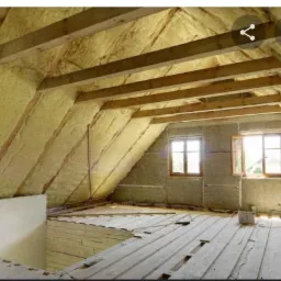 Poddasze z drewnianą konstrukcją dachu i oknami, ocieplone wełną mineralną, widoczne deski podłogowe w trakcie prac wykończeniowych.