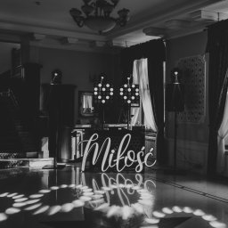 Przemysław Walkowski - Czarno-białe zdjęcie sali balowej z dekoracją świetlną 'Miłość', reflektorami i nagłośnieniem, przygotowanej na wesele. Parkiet odbija światło.