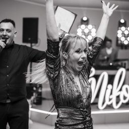 Przemysław Walkowski - Czarno-białe zdjęcie z mikrofonem konferansjera i rozentuzjazmowanej kobiety na tle sceny z napisem 'Miłość' i oświetleniem, uchwycone w trakcie imprezy.