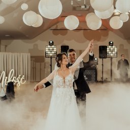 Przemysław Walkowski - Para młoda tańczy pierwszy taniec w dymie, oświetlona światłami i lampionami. W tle widoczne nagłośnienie i napis 'Miłość' z neonu.