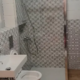 Wykończona łazienka z kabiną prysznicową, umywalką i toaletą, wyłożona płytkami w geometryczne wzory, z drewnopodobną podłogą.