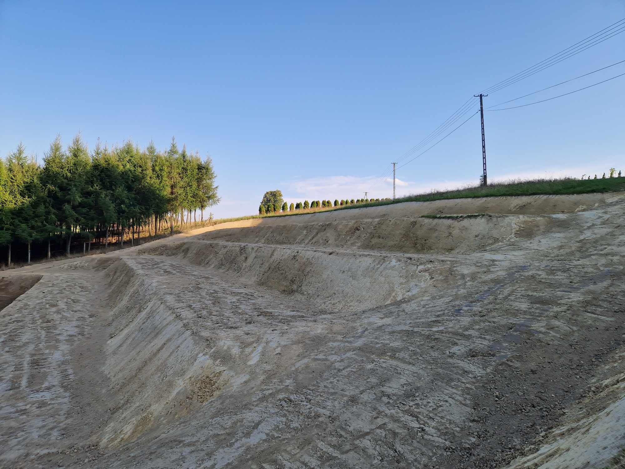 Przygotowany teren pod budowę w Podegrodziu, widoczne warstwy ziemi po wykopie, w tle linia drzew i słupy energetyczne.