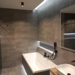 Nowoczesna łazienka w szarościach z podświetlaną wanną, umywalką nablatową na drewnianym blacie i czarną armaturą.