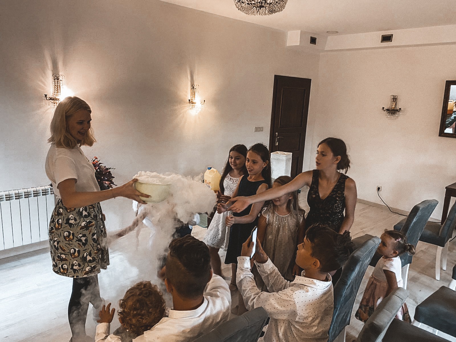 Animator w spódnicy w pandy prezentuje dzieciom widowiskowy pokaz z dymiącą misą na tle jasnego wnętrza.