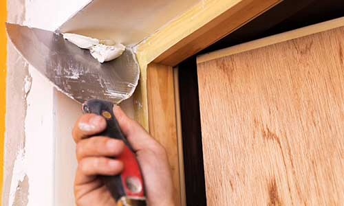 Wyrównywanie szpachlą narożnika ościeżnicy przed montażem drzwi przesuwnych z drewnianą okleiną.