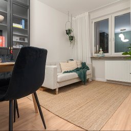 R.A HONEST PARTNERS SPÓŁKA Z.O.O - Jasne wnętrze: sofa z poduszkami i pledem, dywan z juty, okno z zasłonami, czarne krzesła przy drewnianym stole. Rośliny doniczkowe dodają przytulności.