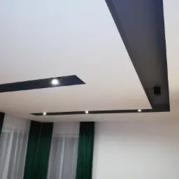 Nowoczesny sufit podwieszany z czarnymi elementami i punktowym oświetleniem LED, widoczne zielone zasłony w oknie.