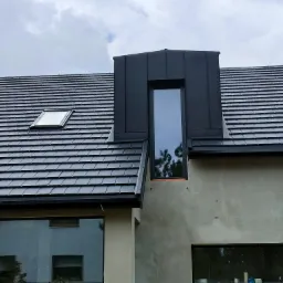 Nowoczesny dom z czarną dachówką ceramiczną, oknem dachowym i lukarną w czarnym metalu, elewacja w stanie surowym.