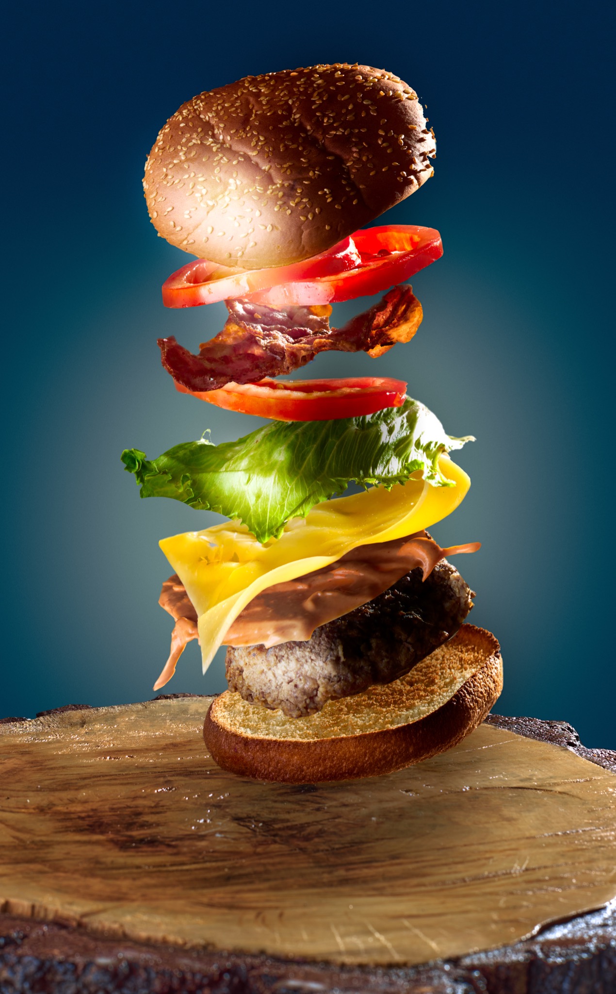 Latający hamburger z bekonem, serem, pomidorem i sałatą na drewnianej desce na tle niebieskiego gradientu.