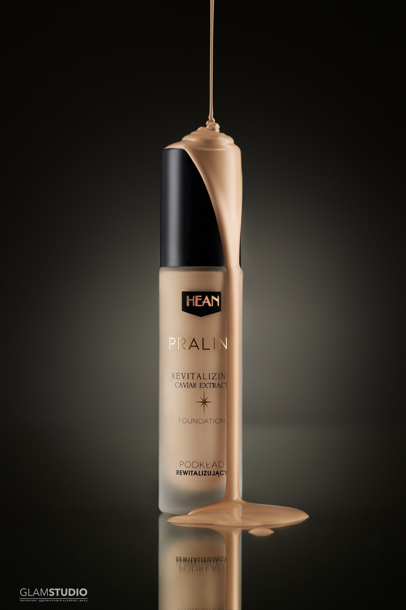 Butelka podkładu HEAN Pralin z kapiącą, beżową cieczą na czarnym, błyszczącym tle, podkreślającym luksusowy charakter produktu.