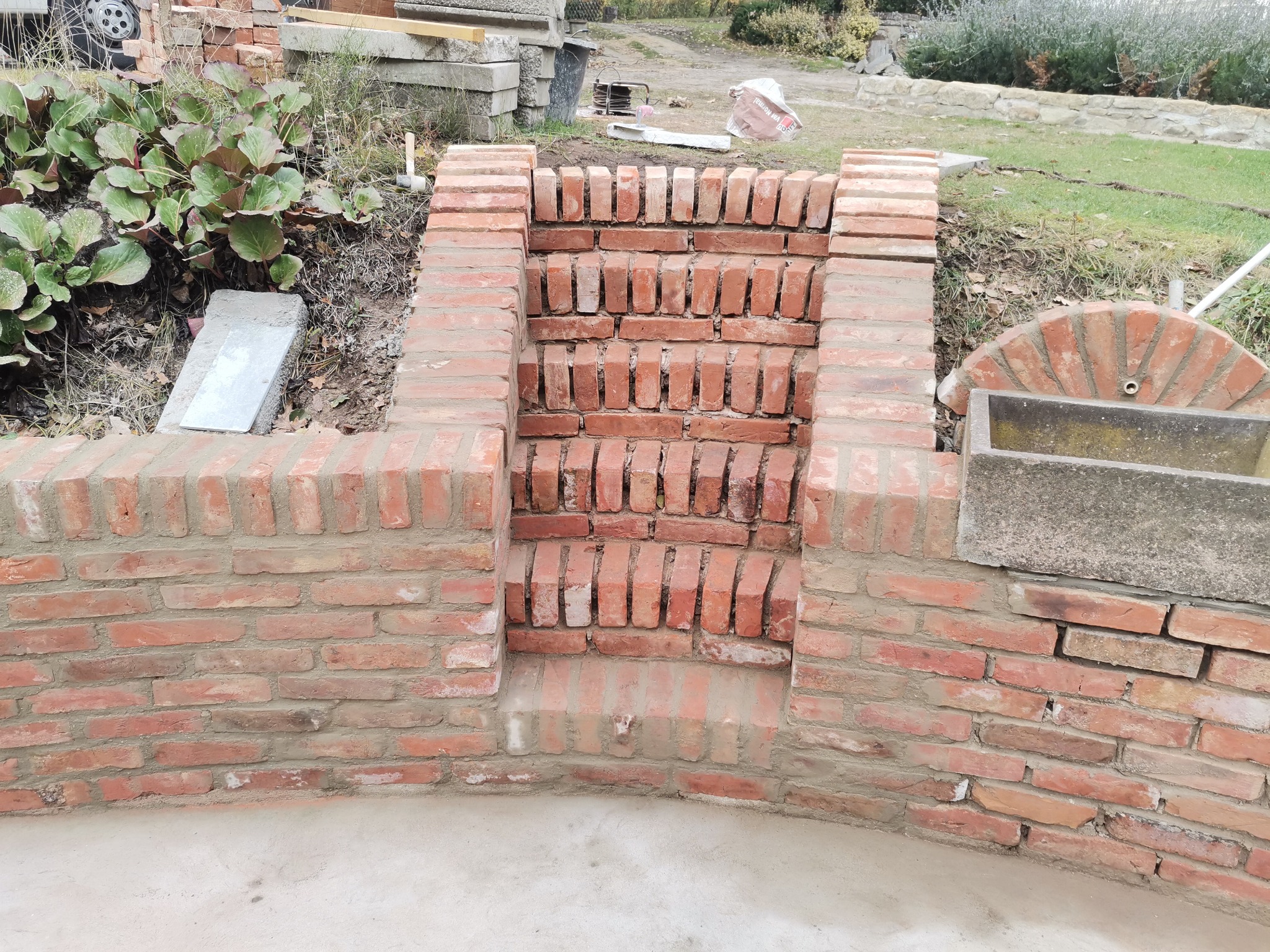 Budowa schodów z czerwonej cegły na zewnątrz, widoczny etap prac murarskich, z elementami krajobrazu w tle.