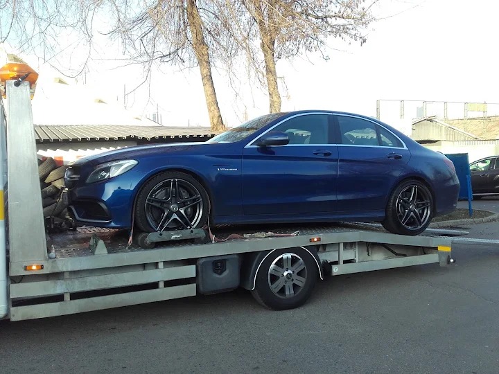 Niebieski Mercedes-Benz C63 AMG na lawecie z oponami zabezpieczającymi za kabiną, widok z boku, oświetlenie dzienne.