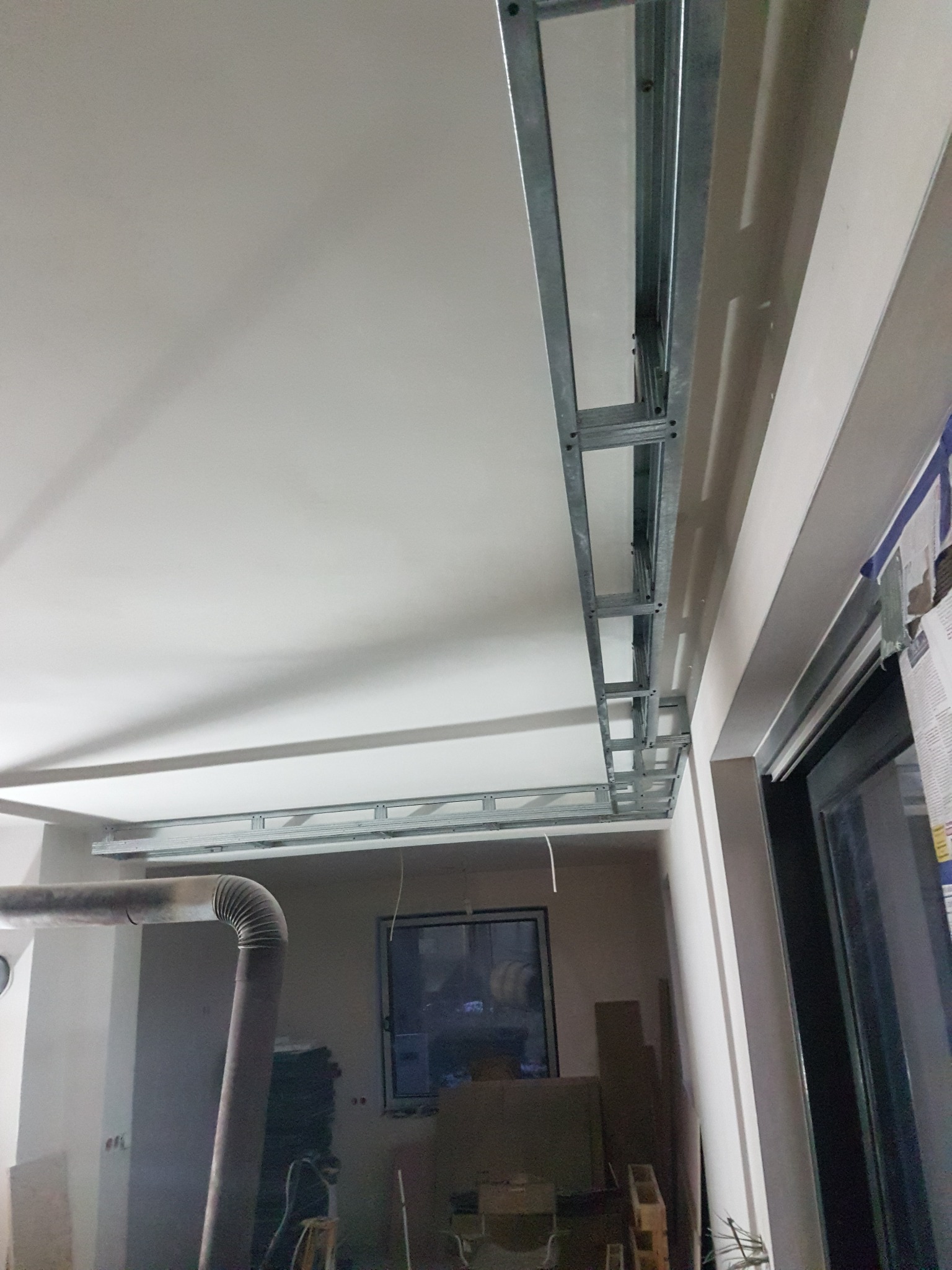 Montaż metalowego stelażu sufitowego pod płytę gipsowo-kartonową, widoczny fragment instalacji wentylacyjnej i okno w tle.