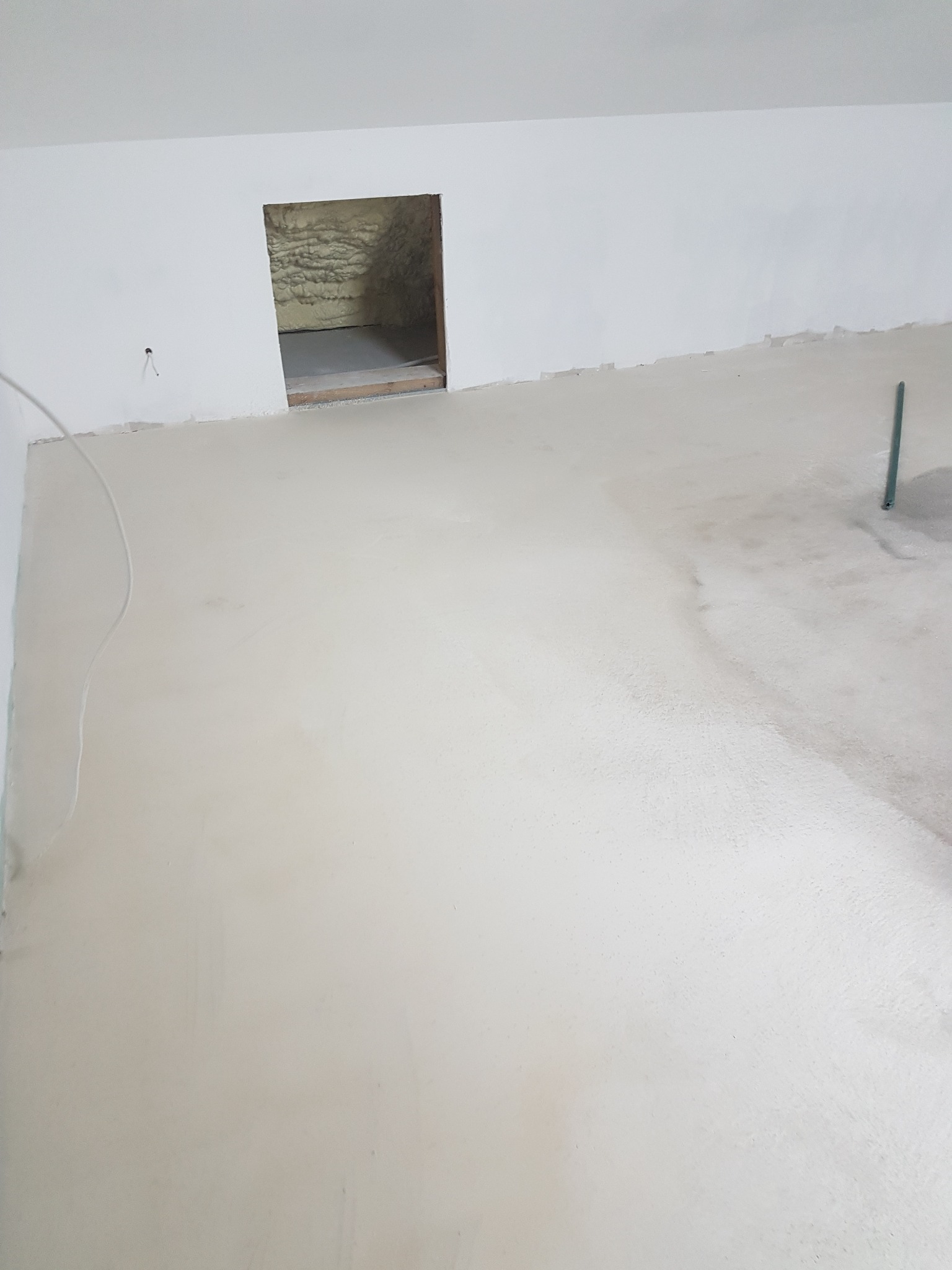 Wnętrze w trakcie prac wykończeniowych w Górze Kalwarii: świeżo wylana, jasna wylewka na podłodze i otwór w ścianie z widoczną izolacją z pianki.
