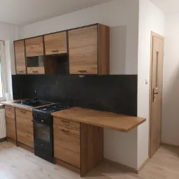 Nowoczesna kuchnia z drewnianymi frontami szafek i czarnym panelem nad blatem, wyposażona w czarną kuchenkę gazową i zlew.