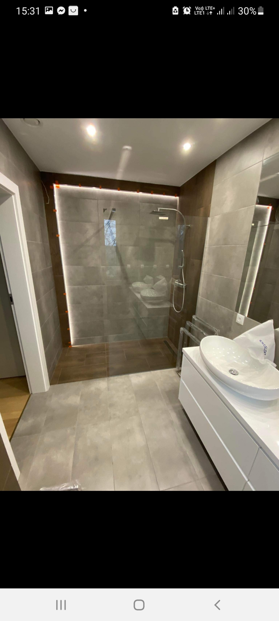 Nowoczesna łazienka po remoncie z kabiną prysznicową typu walk-in, szarymi płytkami i umywalką nablatową na białej szafce.