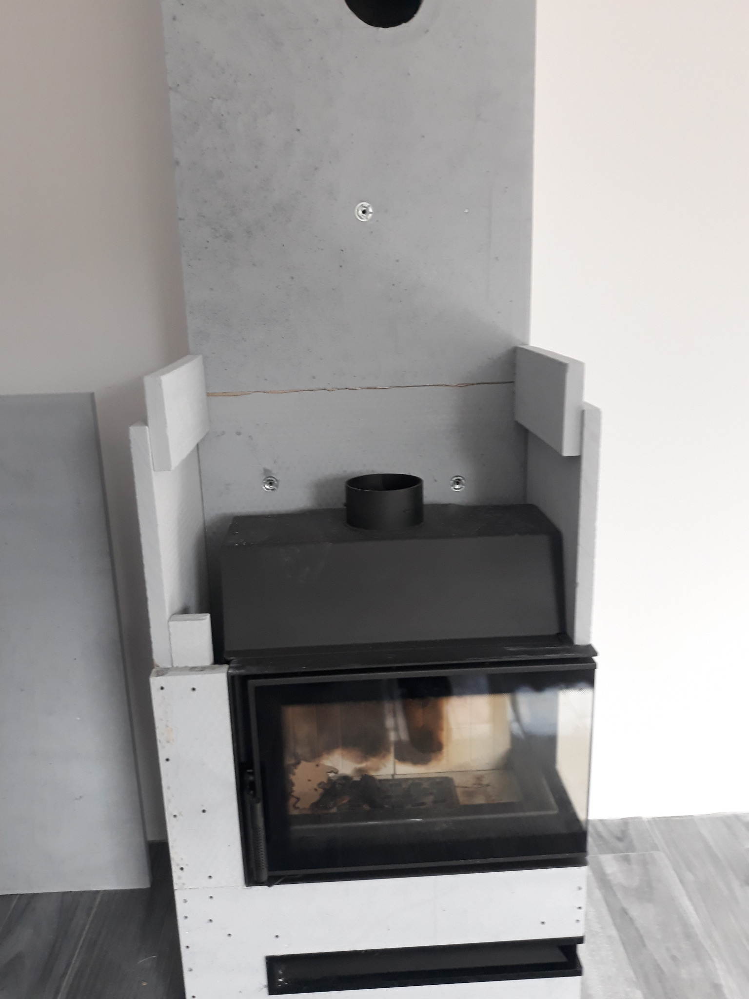 Wnętrze kominka w trakcie obudowy z płyt gipsowo-kartonowych, widoczne mocowania i rura odprowadzająca dym, surowy stan wykończenia.