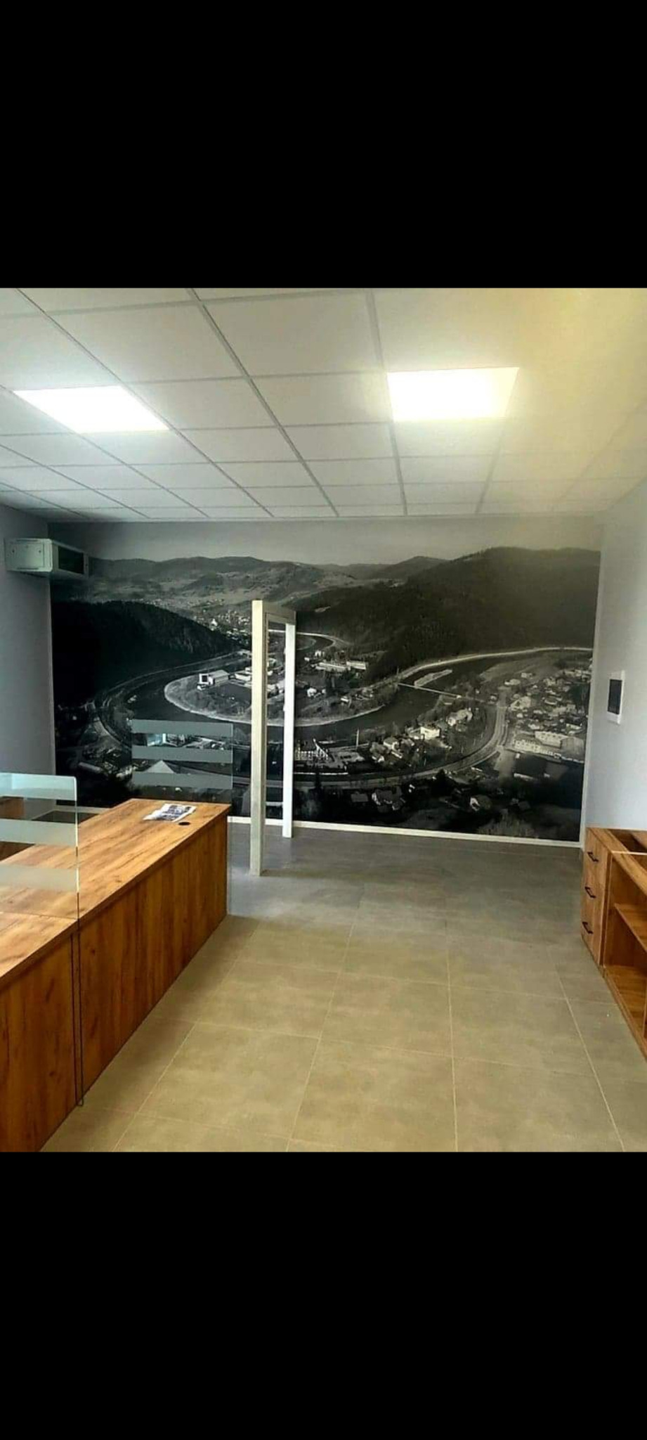 Wnętrze biura z drewnianymi meblami i fototapetą przedstawiającą krajobraz górski z zakolem rzeki.