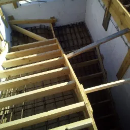 Zbrojenie fundamentu przygotowane do zalania betonem, widoczne drewniane szalunki i izolacja pionowa ścian fundamentowych.