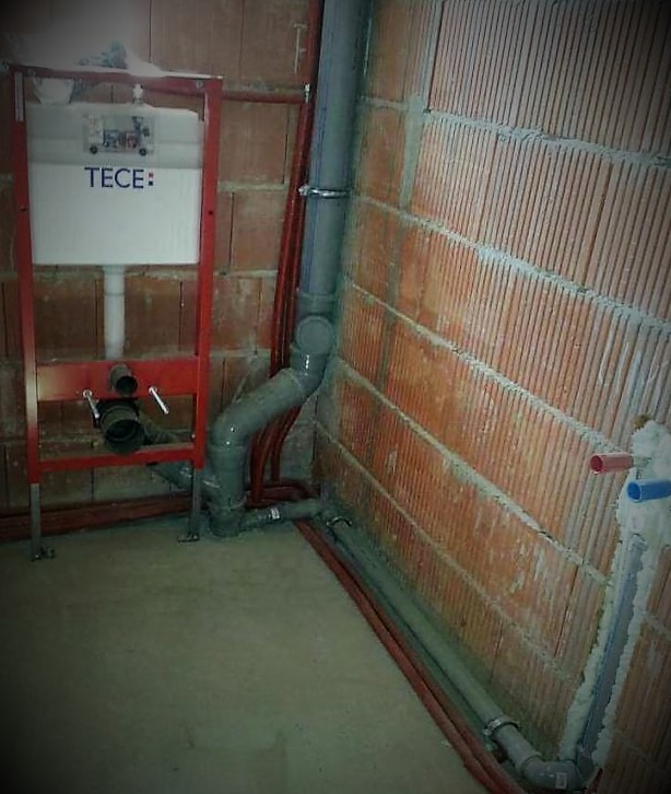 Montaż stelaża podtynkowego TECE z widocznymi rurami kanalizacyjnymi i instalacją wodną w surowym stanie, ściana z cegły dziurawki.