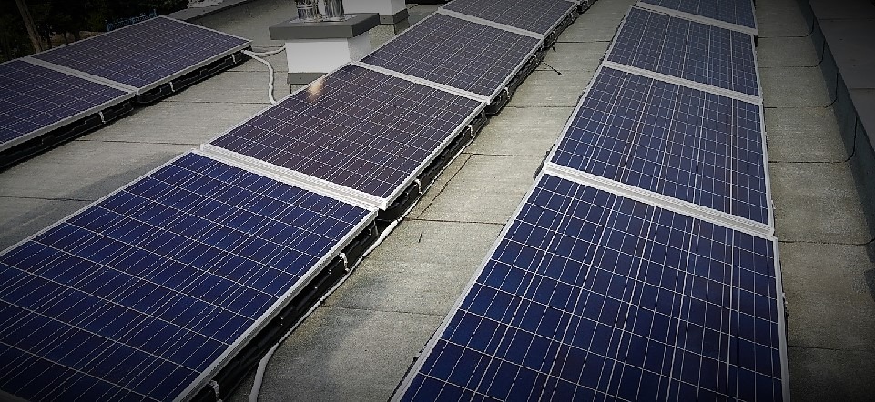 Instalacja paneli słonecznych na płaskim dachu w Toruniu, widok z góry, szare panele dachowe, srebrne ramy paneli fotowoltaicznych.