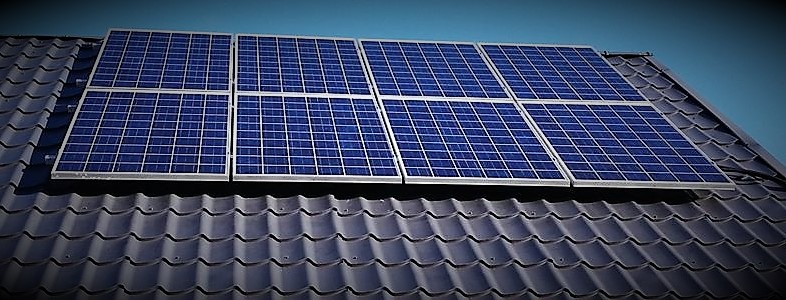 Panele fotowoltaiczne, niebieskie, zamontowane na dachu z ciemnej dachówki, widok z dołu pod kątem.