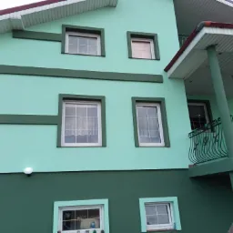 Dwukolorowa elewacja domu w odcieniach zieleni z balkonem z ozdobną, metalową balustradą.