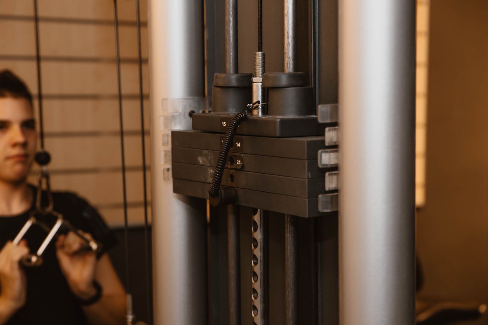 Mężczyzna w czarnej koszulce ćwiczy na maszynie do ćwiczeń na siłowni, z widocznymi obciążeniami ustawionymi na numer 15.