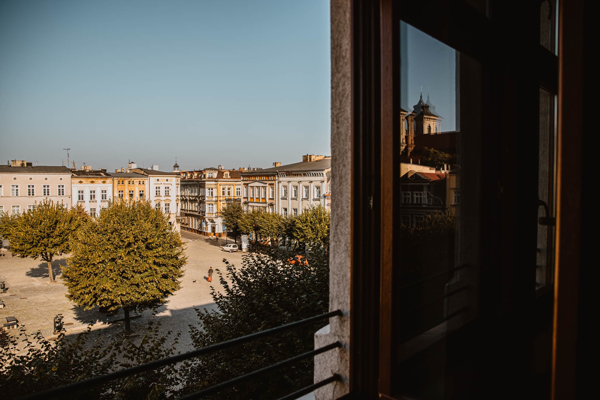 Widok na miejski rynek z okna, z widoczną osobą w pomarańczowych butach spacerującą po placu