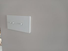 Biały panel z trzema przełącznikami na gładkiej, szarej ścianie, widoczne delikatne cienie.