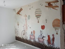 Ściana pokoju dziecięcego z tapetą w pastelowe balony, samoloty i zwierzęta na tle jasnej, niepomalowanej ściany.