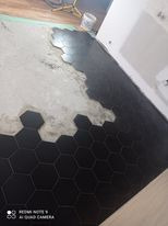 Układanie czarnych, sześciokątnych płytek na podłodze. Widoczny fragment podłoża przygotowanego pod płytki oraz wiaderko z klejem w tle.